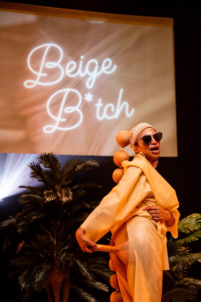 Nima Séne glances over her shoulder beneath a glowing Beige B*tch projection, palm trees behind