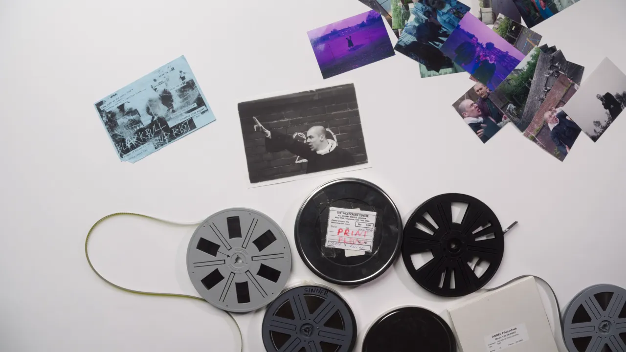 Overhead view of 16mm film reels, cans and scattered photographs from the archive on a white tabletop