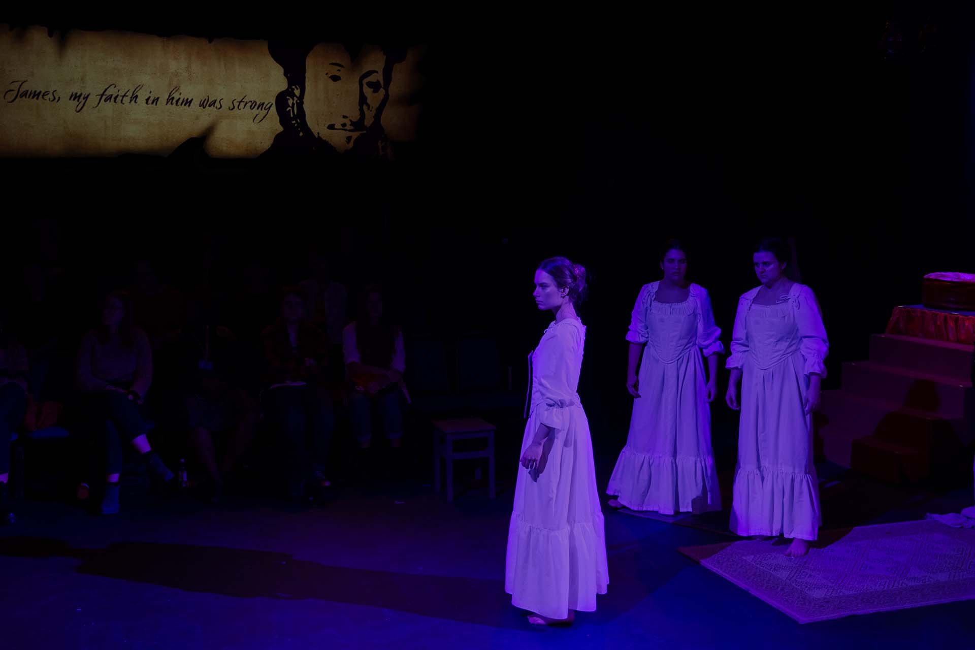 Claire Wetherall, Benedetta Zanetti and Emery Hunter in white gowns beneath a handwritten parchment projection.