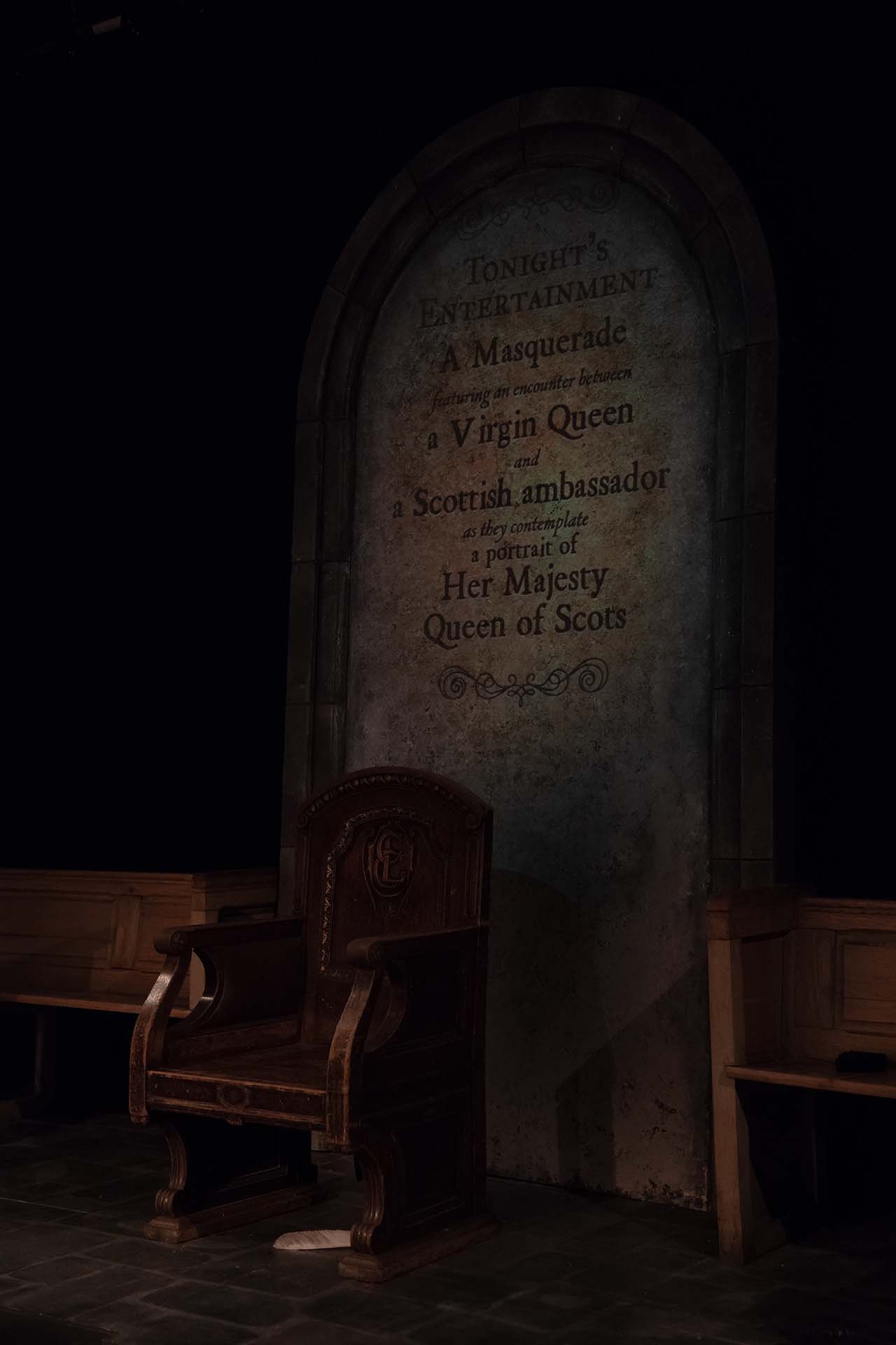 Projection detail: a masquerade playbill projected onto the stone archway above a carved wooden chair.