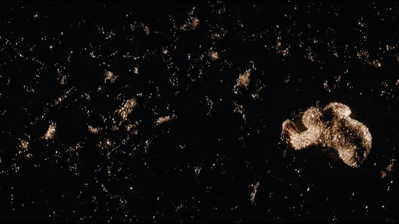 Film still from Grin: glittering tinsel scattered across a black stage floor