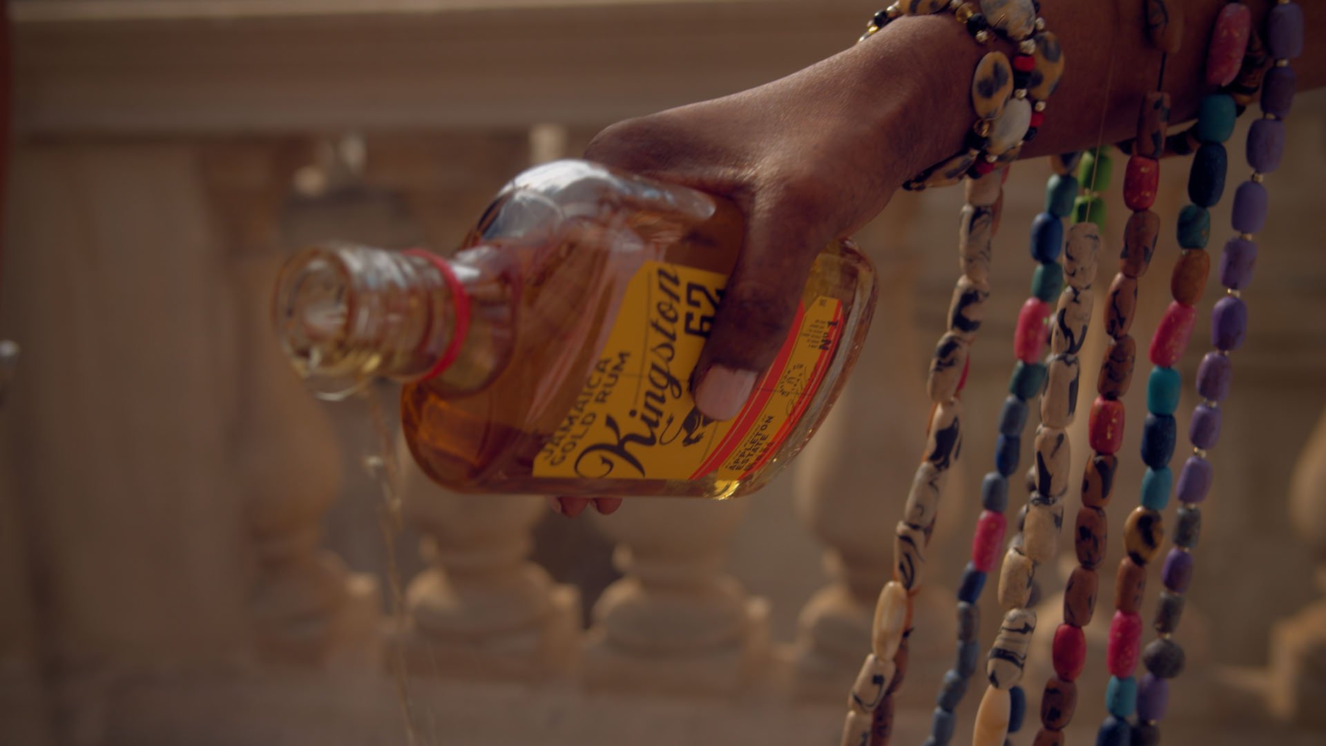 Solariss pours libations from a bottle of Jamaican gold rum, beads draped from her wrist; film still from Lagareh