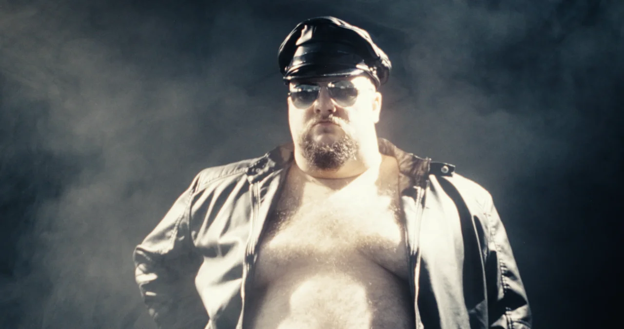 Music video still: man in leather cap, sunglasses and open jacket, bare-chested in swirling smoke
