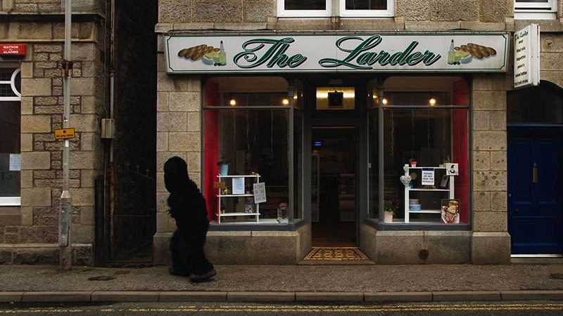 Film still: the Monster walks past The Larder shopfront at dusk in Huntly