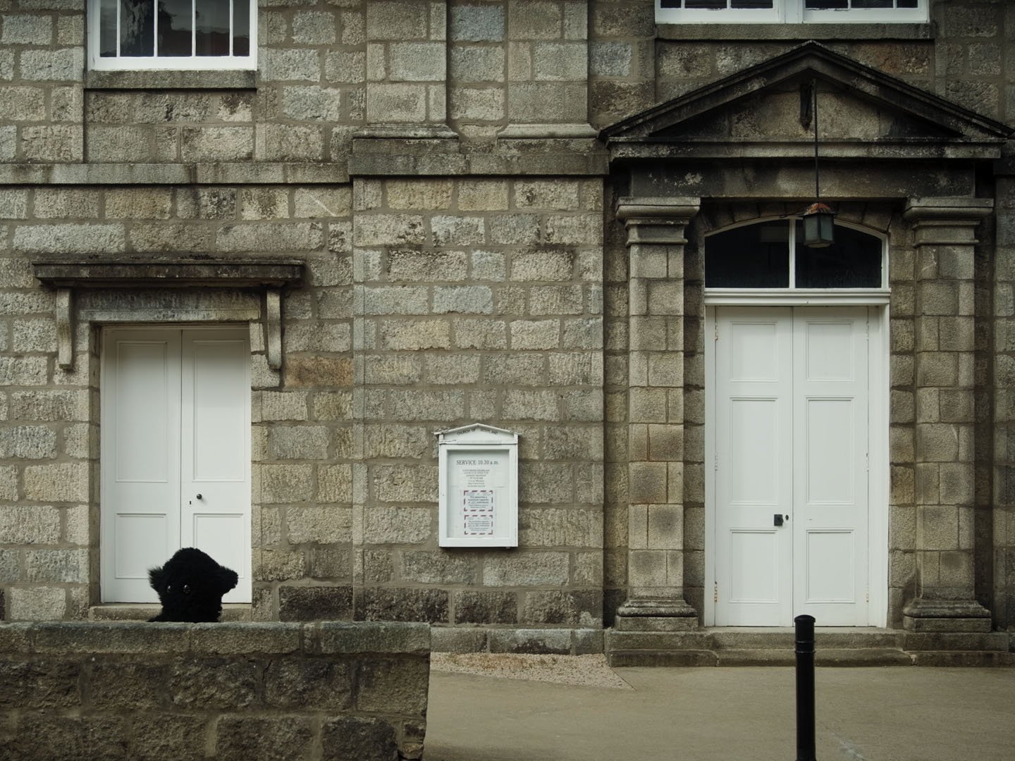 Film still: the dark furry Monster crouches in a white doorway of a granite stone building in Huntly