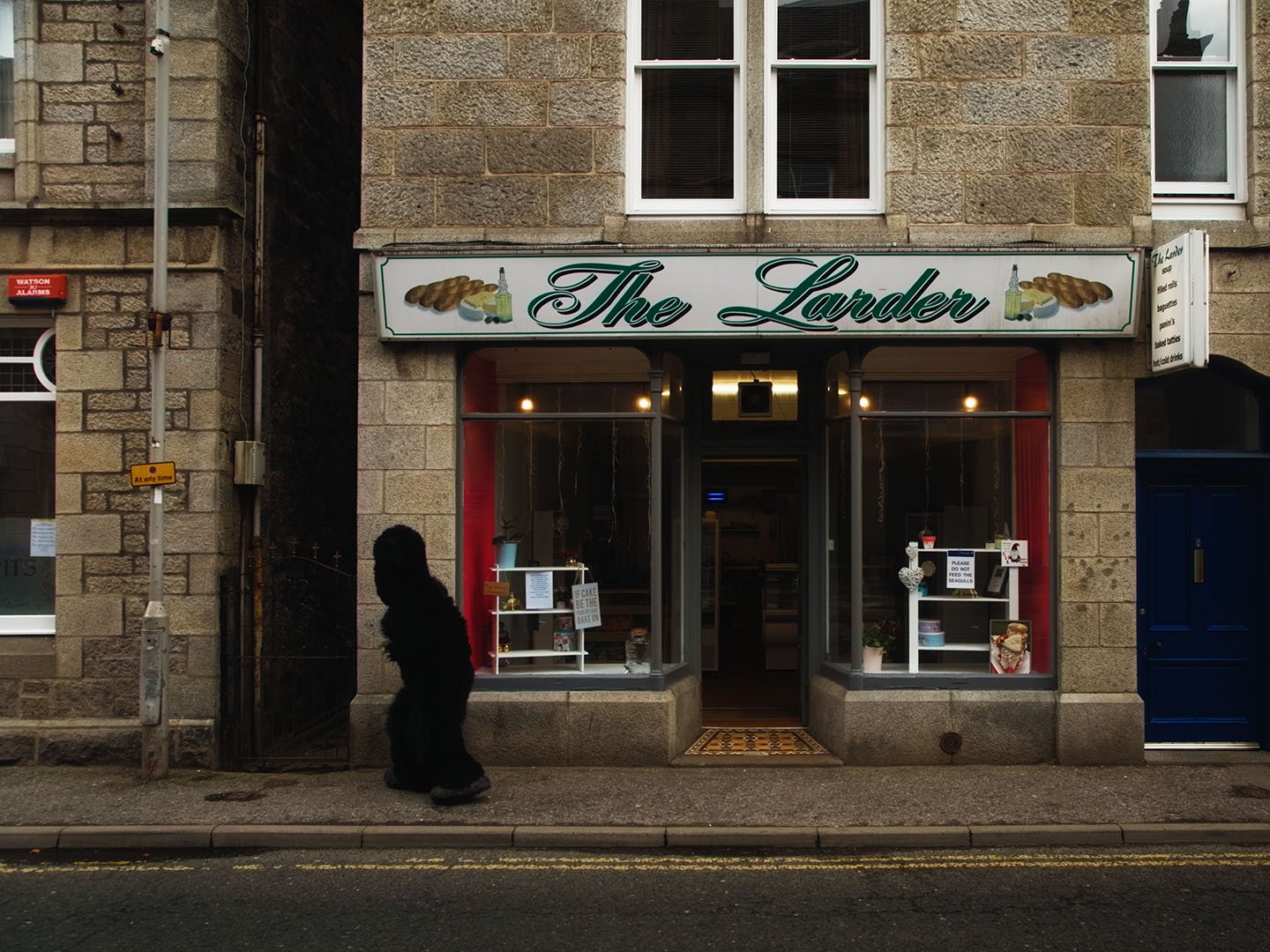 Film still: the Monster walks past The Larder shopfront on a granite Huntly street