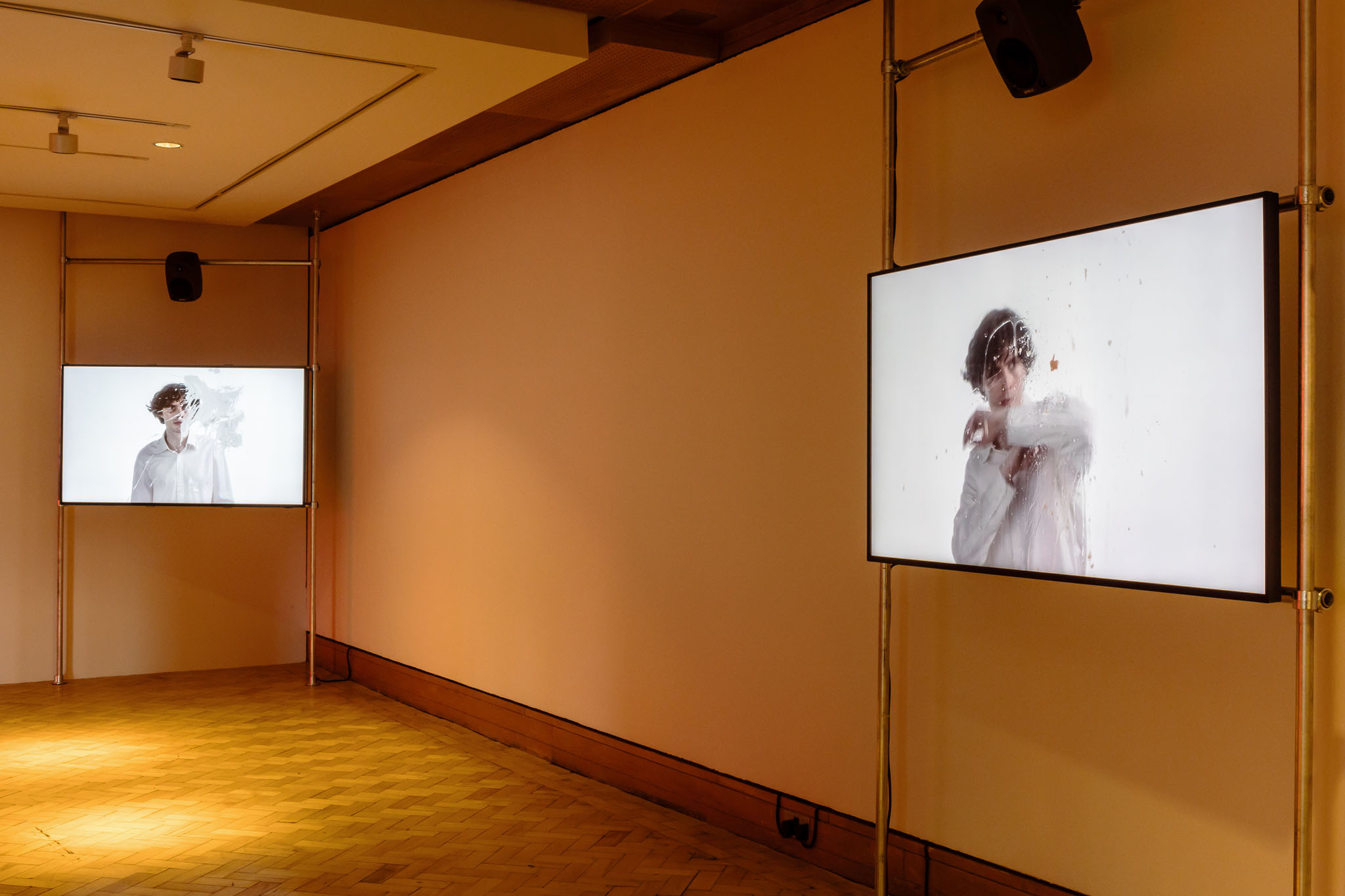 Installation view at City Art Centre, Edinburgh: two screens showing a figure in white behind splattered glass