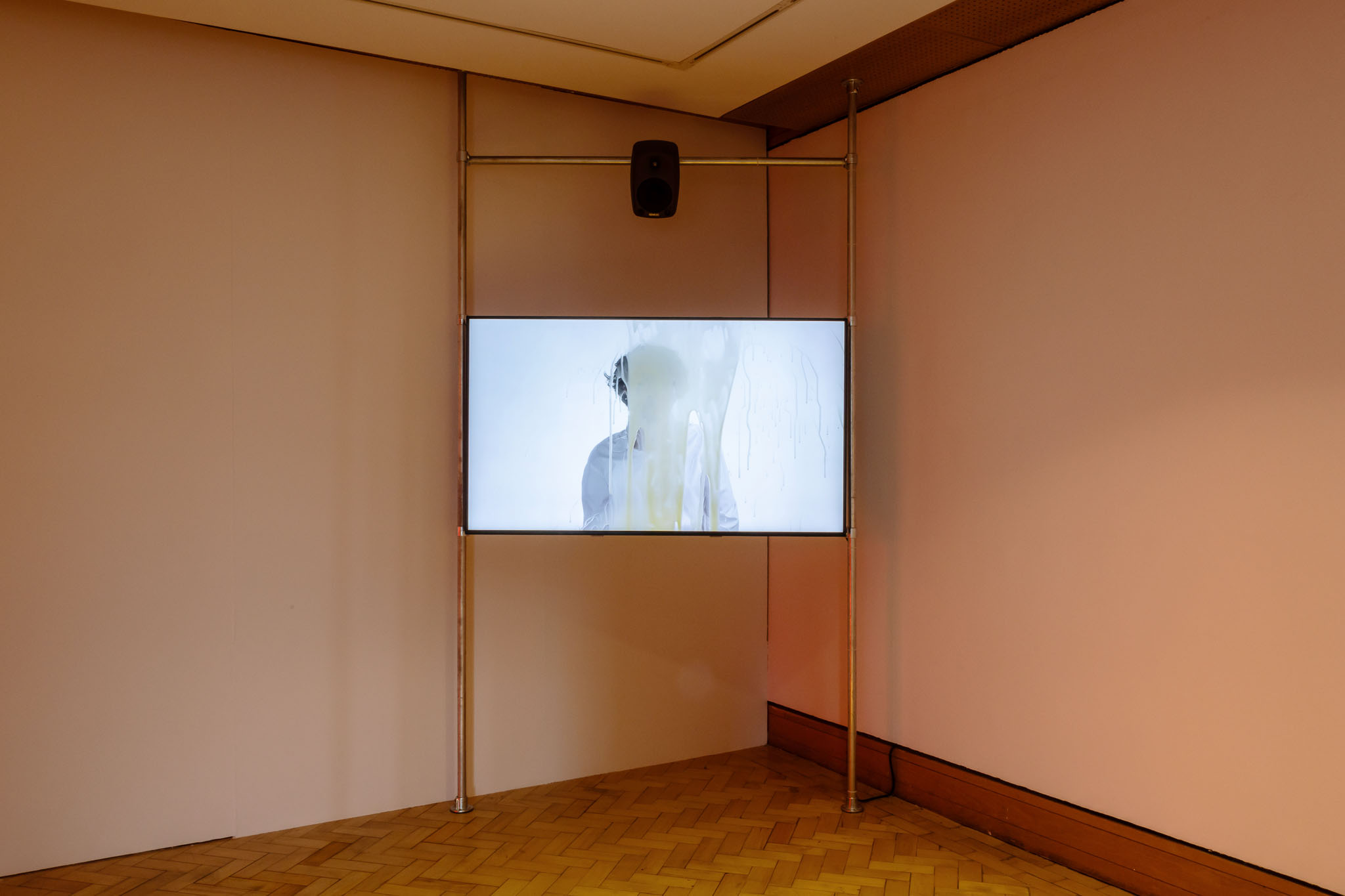 Installation view at City Art Centre, Edinburgh: corner-mounted screen showing a figure behind glass dripping with liquid