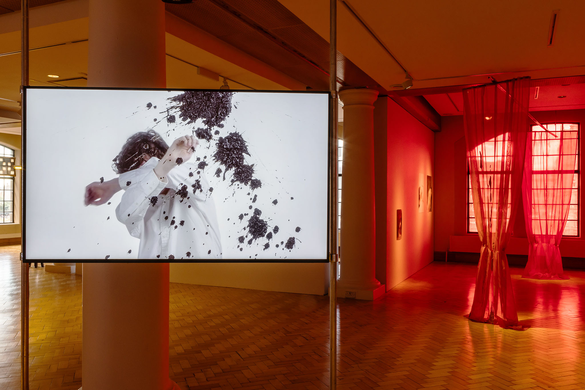 Installation view at City Art Centre, Edinburgh: screen showing a figure dodging flying soil, red curtains behind