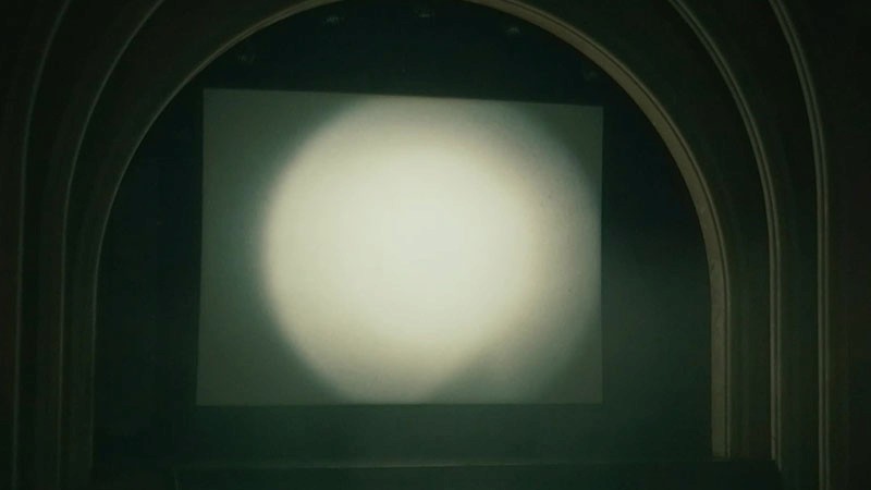 Soft circle of projector light glows on a screen beneath the theatre's arch