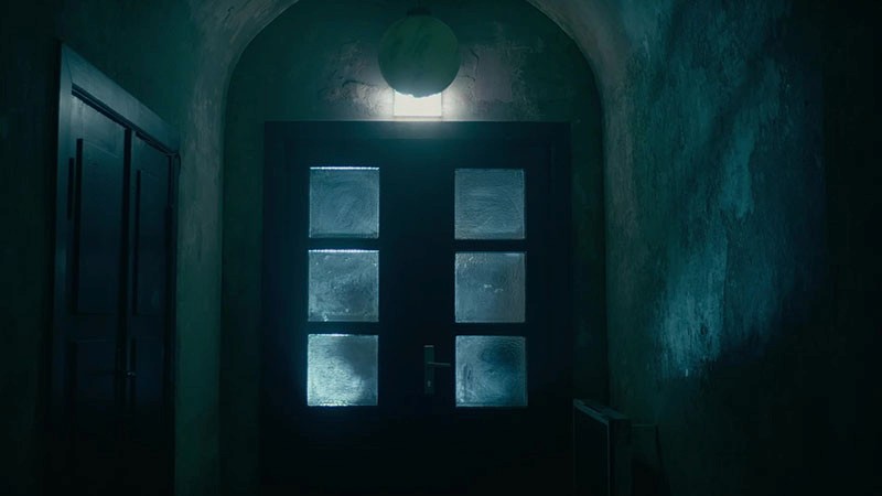 Frosted glass double doors glow blue beneath a globe lamp in a dim corridor