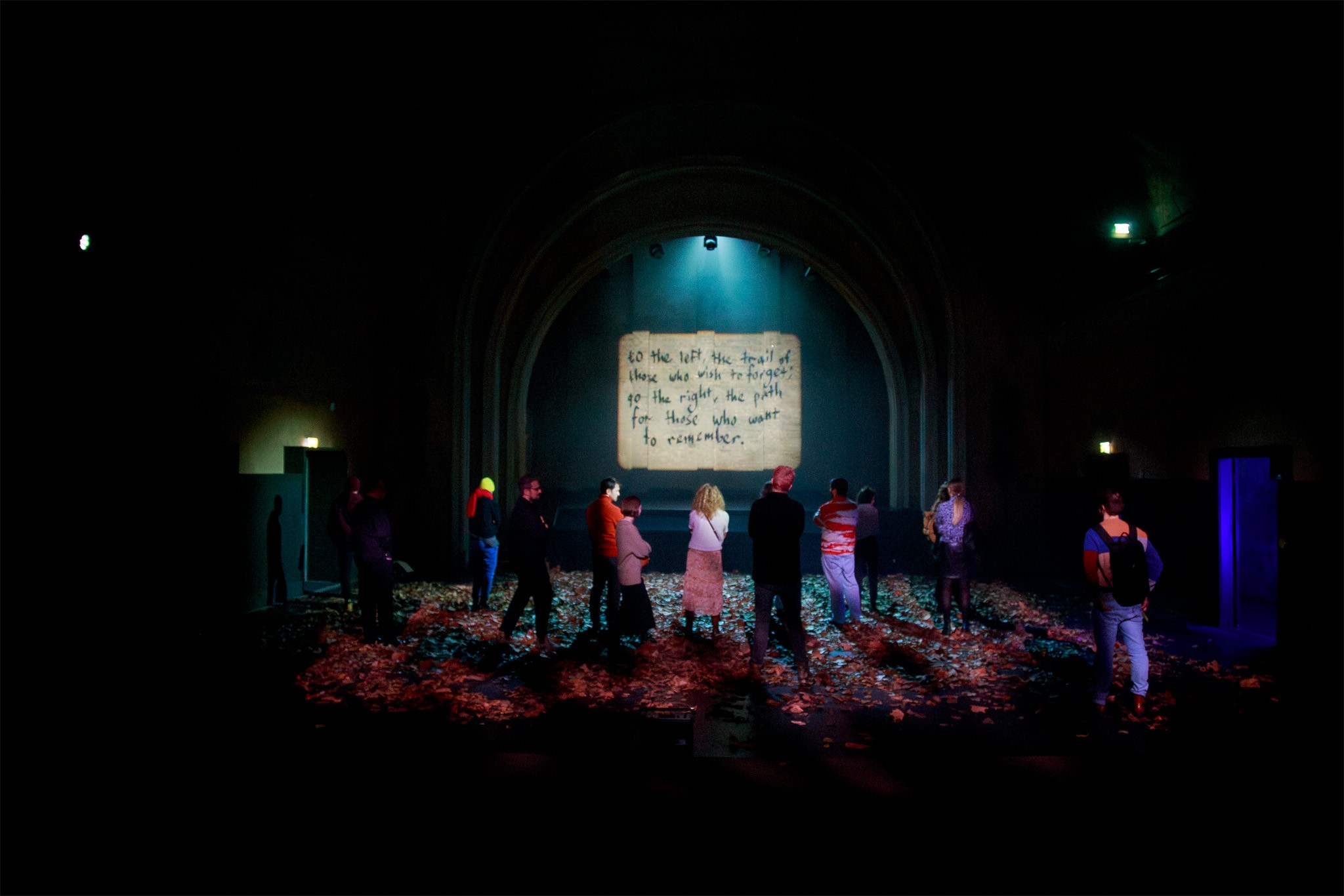 Audience on a leaf-strewn floor watches a handwritten magic lantern projection during the dress rehearsal