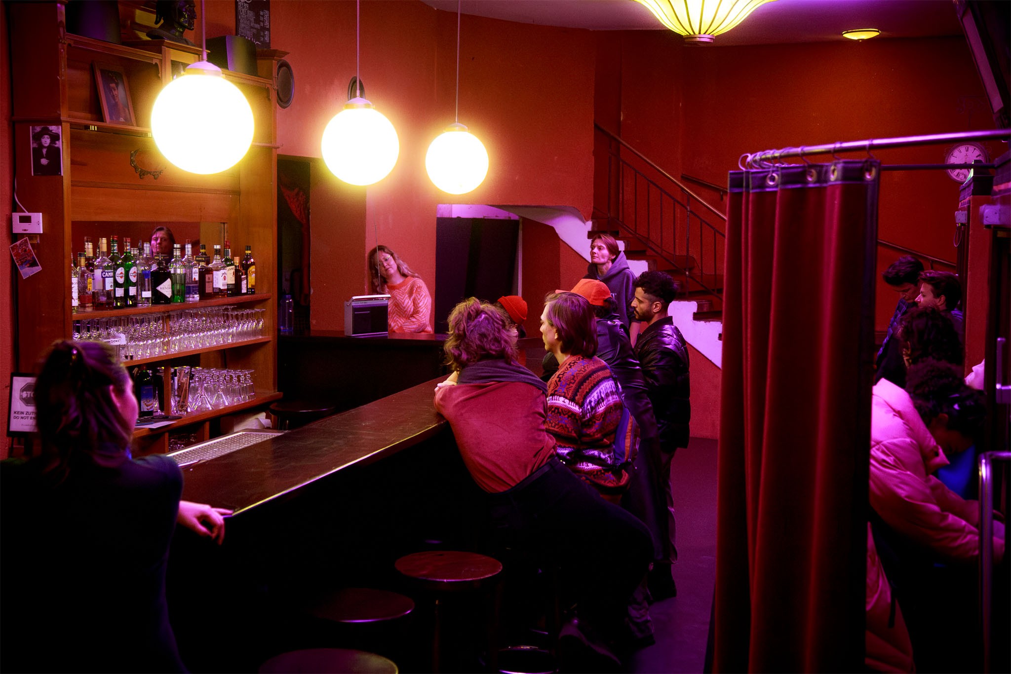 People gather at the warmly lit bar of the Theater im Delphi foyer before a dress rehearsal