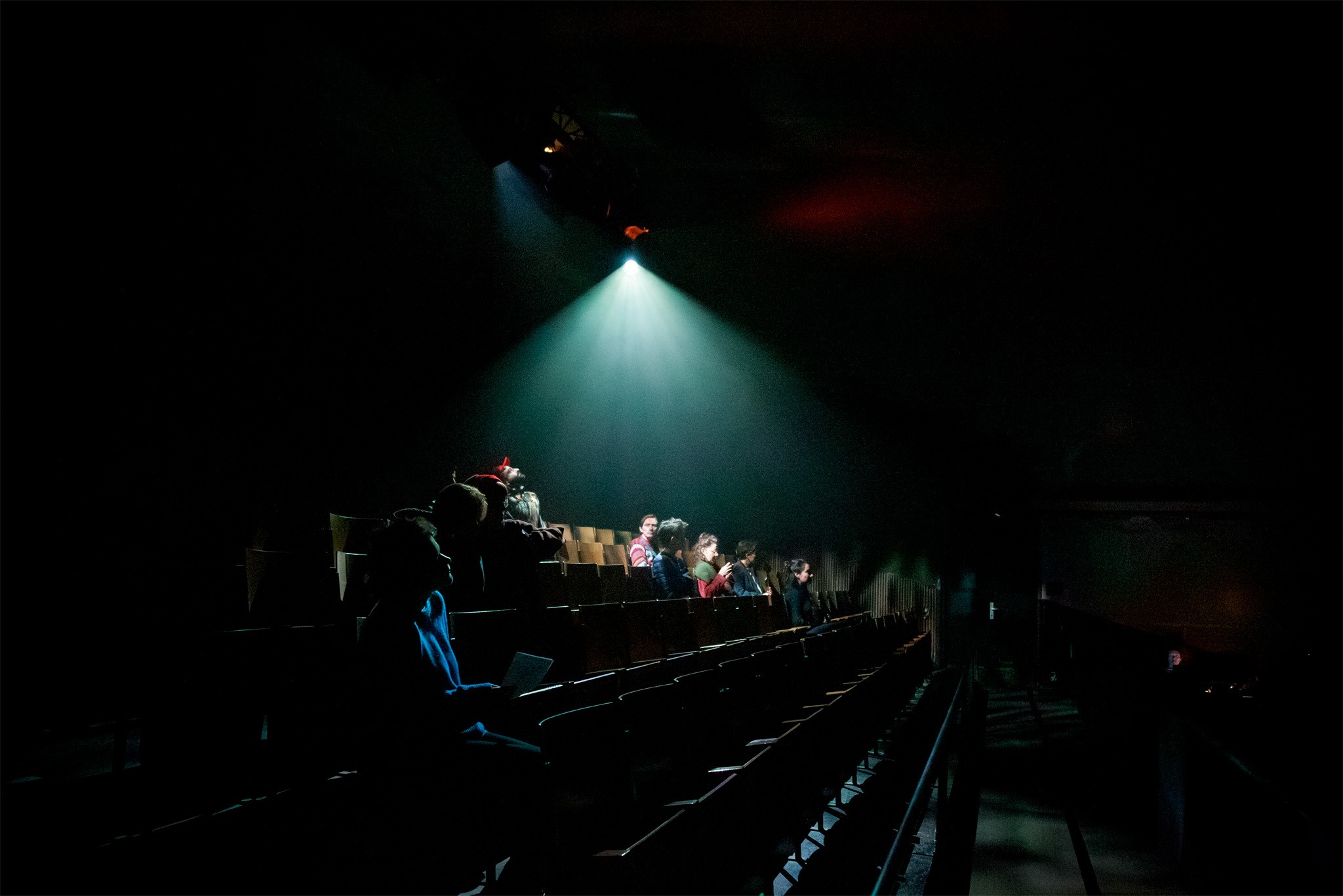Audience members sit in the darkened seating rake beneath a projector beam for the silent film experience