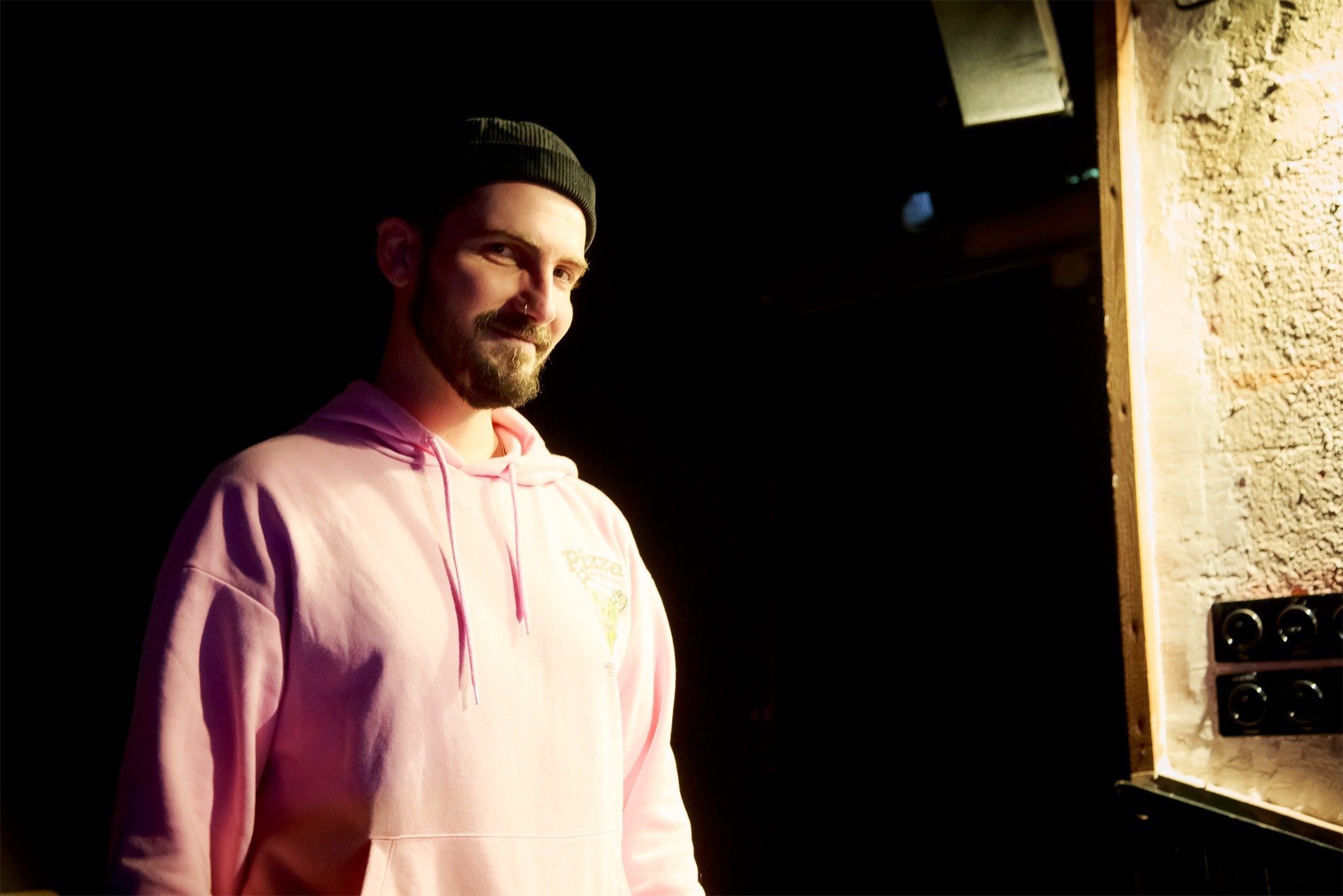 Composer Alexandar Hadjiev in a beanie and pink hoodie, smiling in warm side light