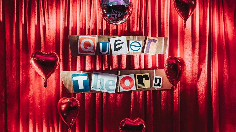 Queer Theory sign in ransom-note lettering on red velvet curtains with heart balloons and a disco ball