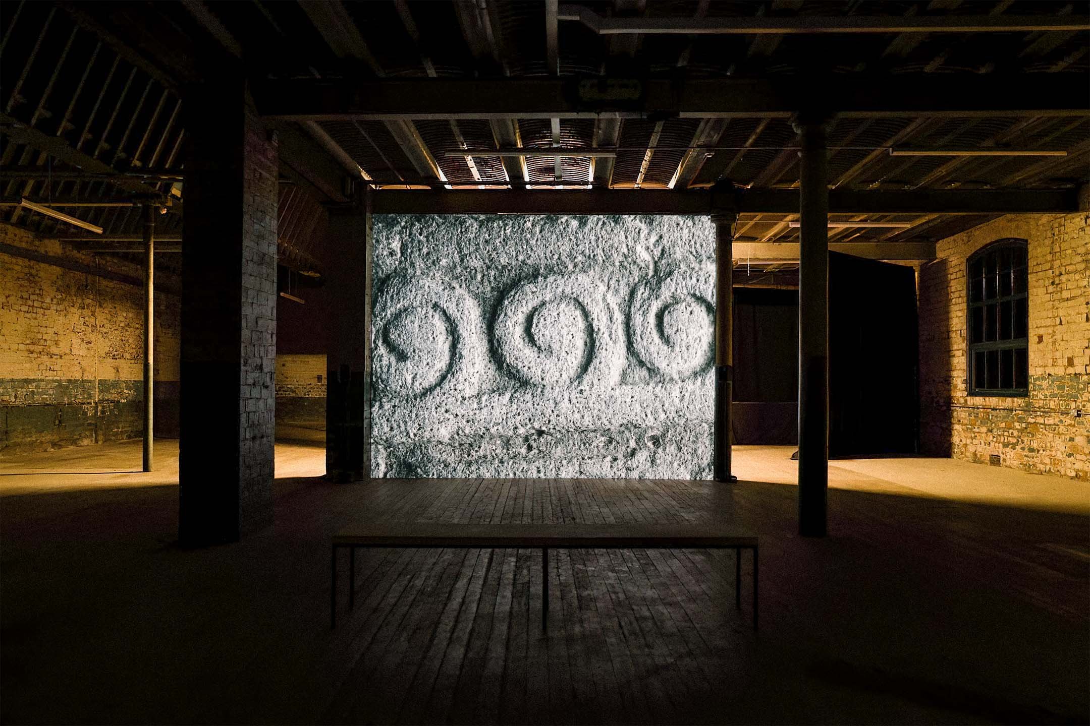 Installation view of Rocabarraigh at Market Gallery, Glasgow: spiral stone carvings projected in a dark brick space