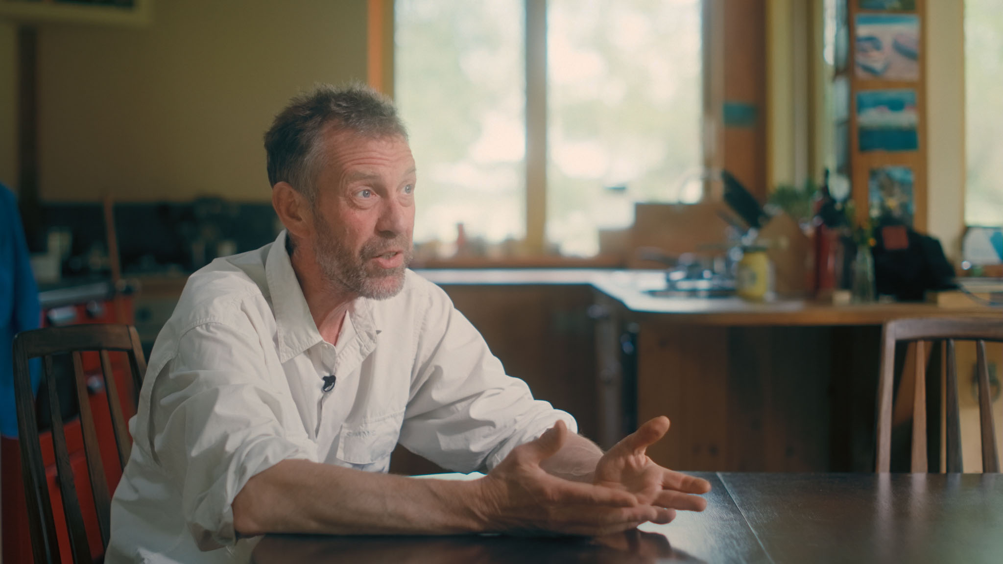 Film still of Al Baker speaking at his kitchen table, gesturing with both hands