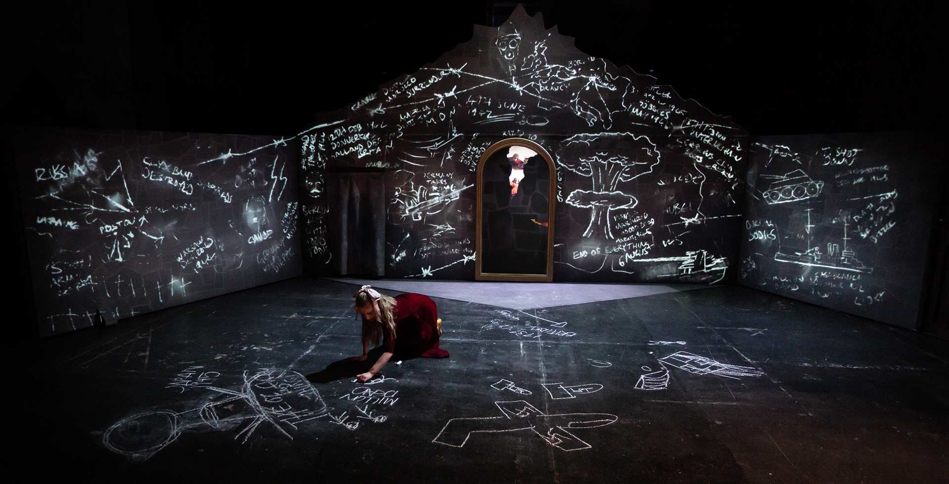Claire Wetherall as Maria crouches drawing in chalk while projected chalk sketches cover the cellar walls.