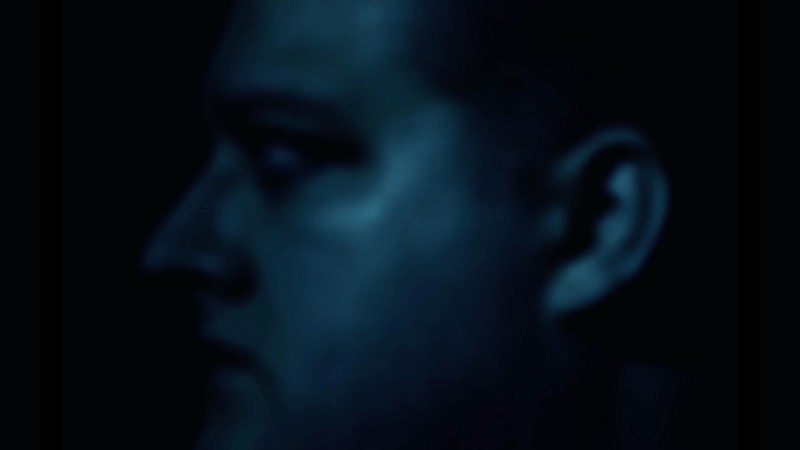 Jamie Black in dark blue profile against blackness, music video still from Tunnel Blue