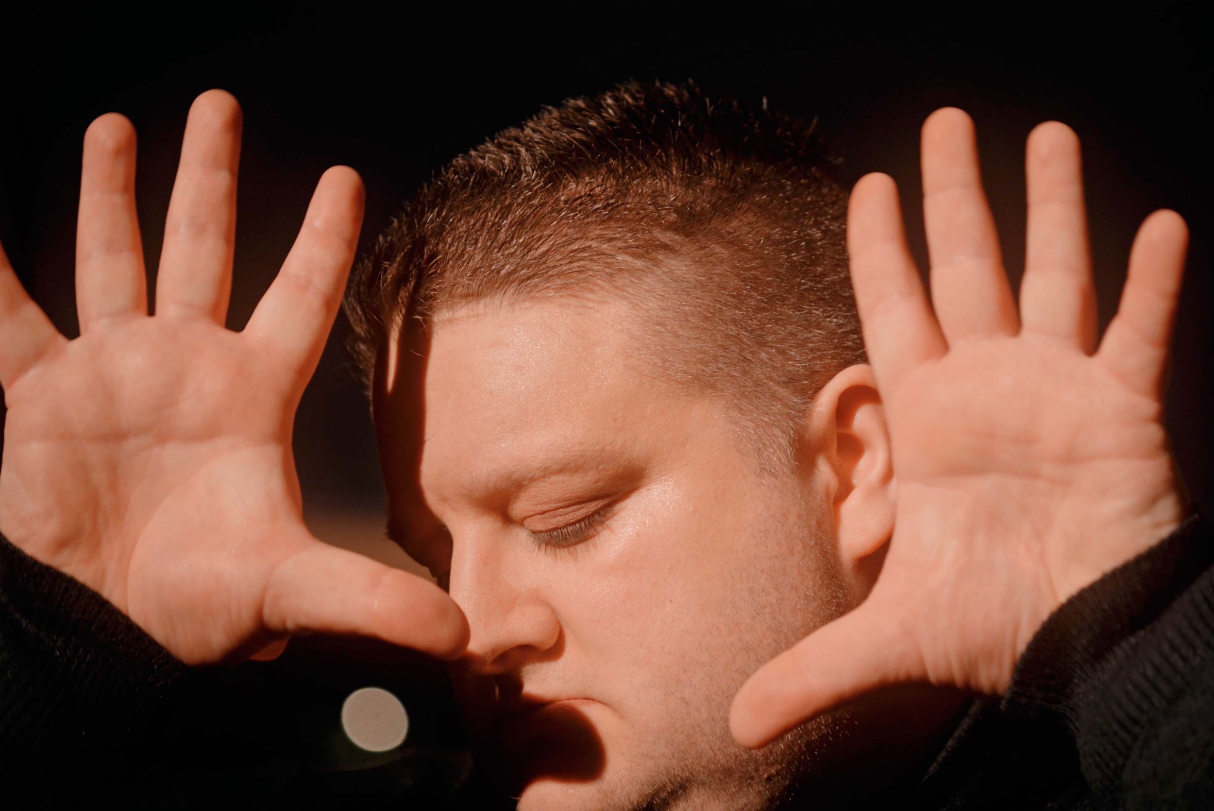 Film still from Tunnel Blue: Jamie Black, eyes closed, holds both palms open beside his sunlit face